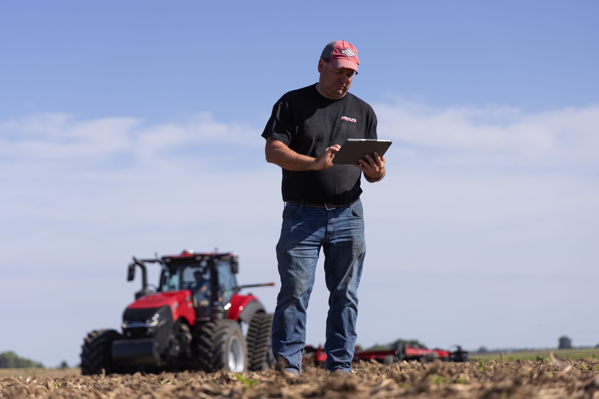 Man in field holding a tablet in front of a Case IH tractor.