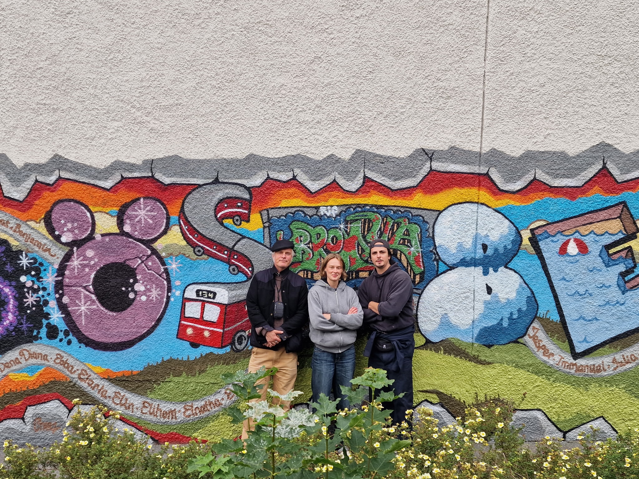 Två män och en kvinna står framför en muralmålning i grafittistil