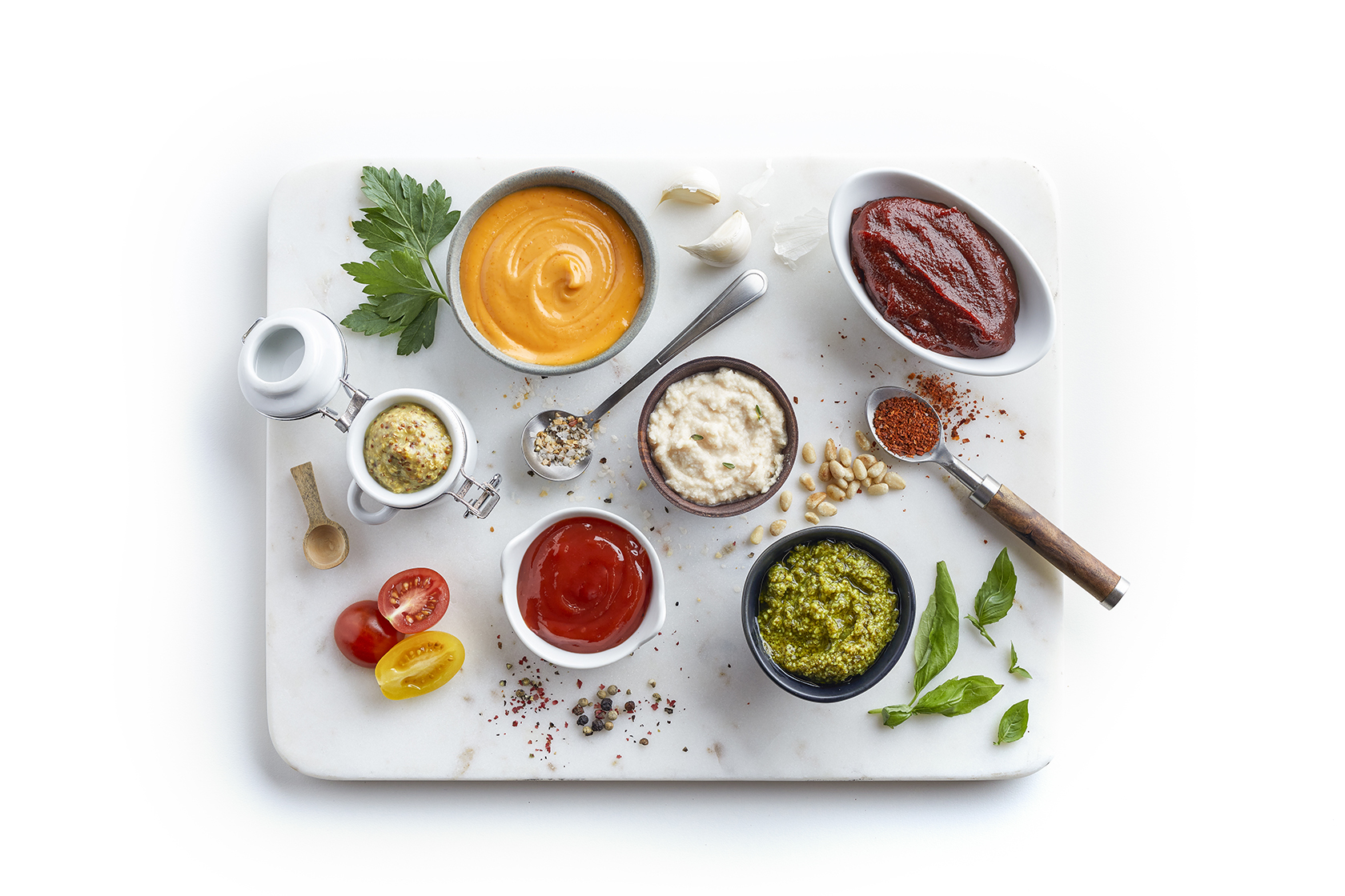 Assorted sauces, garnishes, and ingredients arranged on a marble board, including pesto and ketchup.
