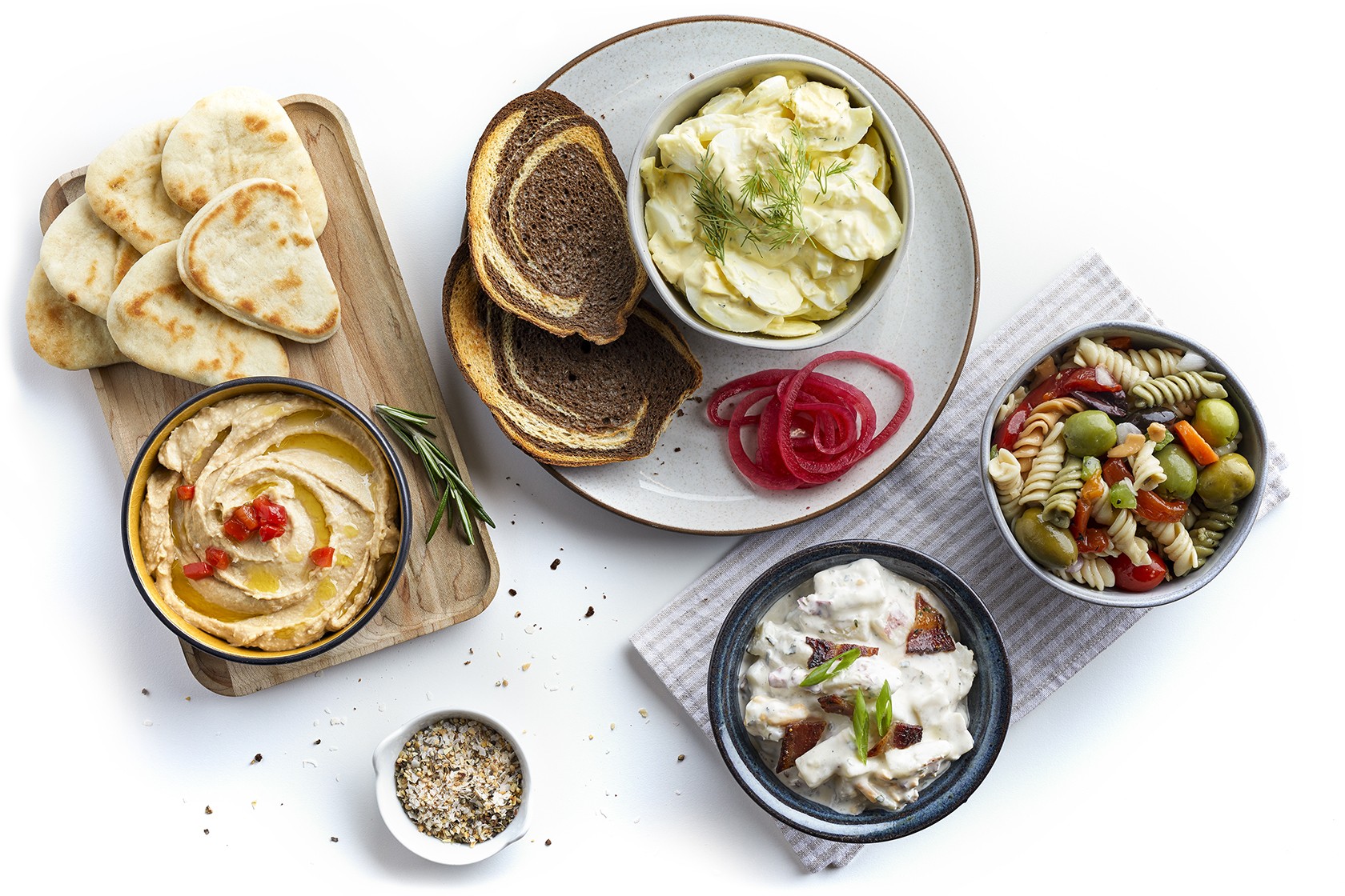 Assorted salads, hummus with pita, rye bread, and pickled onions arranged on a table